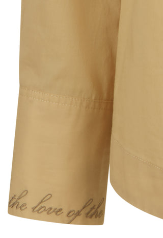 close-up-of-a-beige-or-tan-fabric-garment-sleeve-with-cursive-text-reading-the-love-of-the-printed-near-the-cuff-on-a-white-background