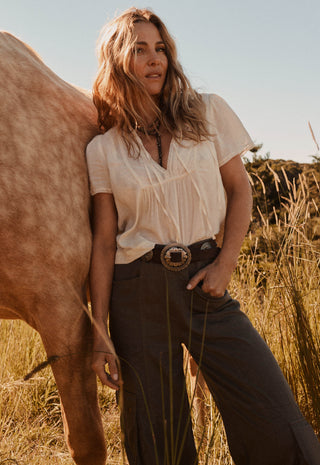 A woman stands outdoors in a field next to a horse