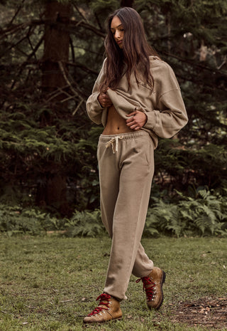 a-woman-wearing-a-matching-beige-cropped-hoodie-and-sweatpants-set-with-brown-lace-up-boots-standing-in-a-grassy-forest-clearing