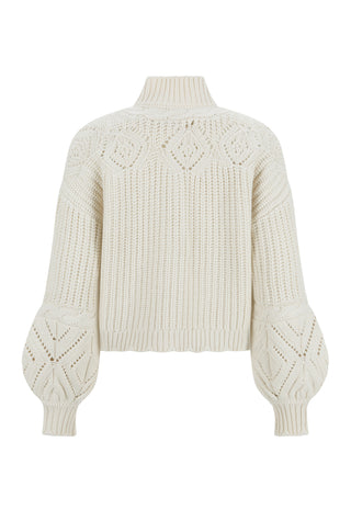 A woman wearing a chunky cable-knit turtleneck sweater in a warm cream/beige color